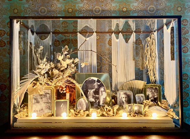 Marc Swanson, Memento Mori, 2022. Vintage display case, artificial flowers, slip, vintage frames, fan, fringe, inkjet prints, lights and lightbulbs, vintage tassels, upholstery tacks, 38 × 28 × 13 inches